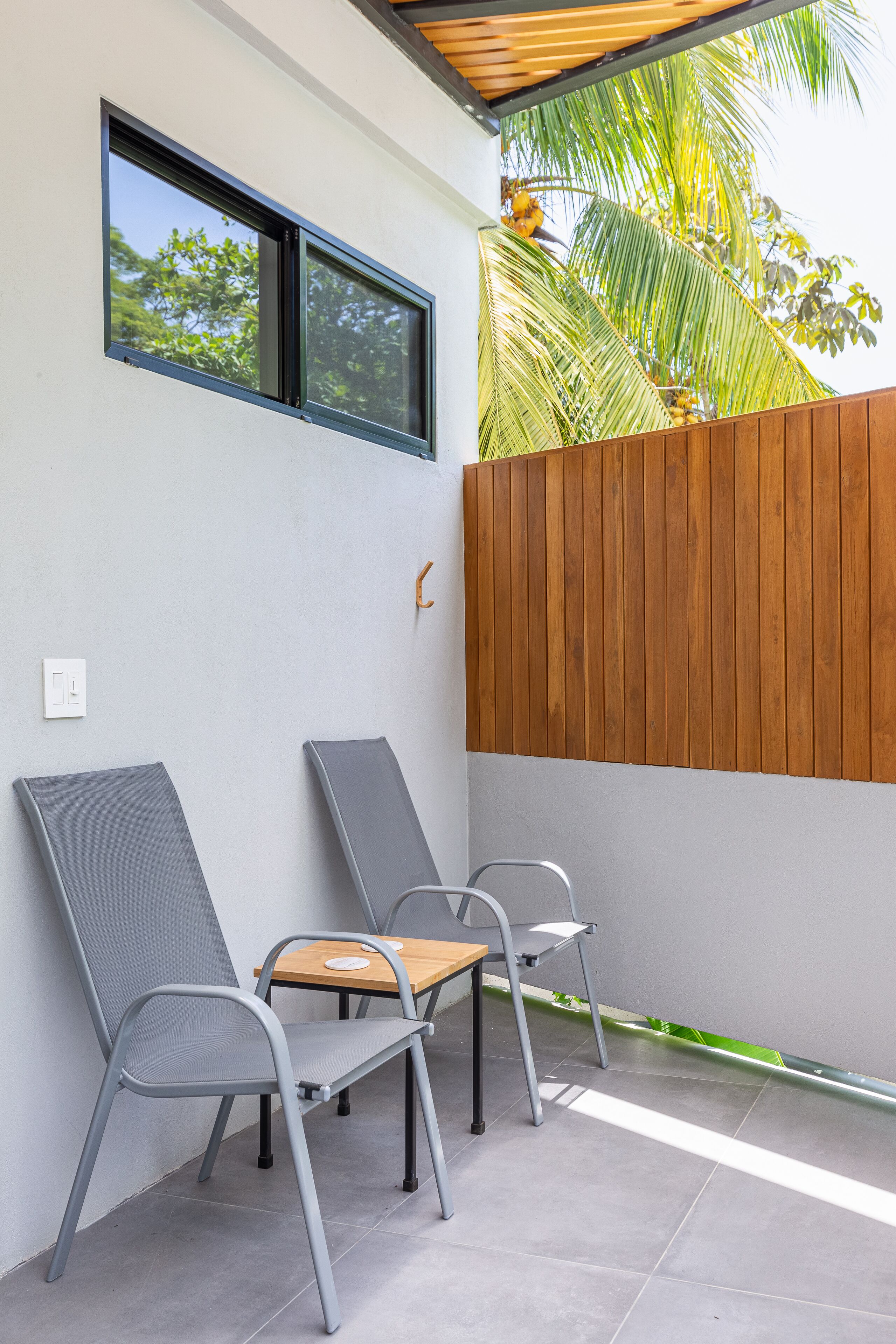 Un patio con dos sillones grises, una pequeña mesa de madera y una valla de madera.