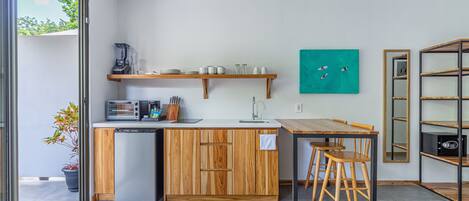 Une cuisine moderne avec des meubles en bois, un lave-vaisselle encastré, un four à micro-ondes et une machine à café. On y trouve une table en bois avec des chaises et une petite plante en pot.