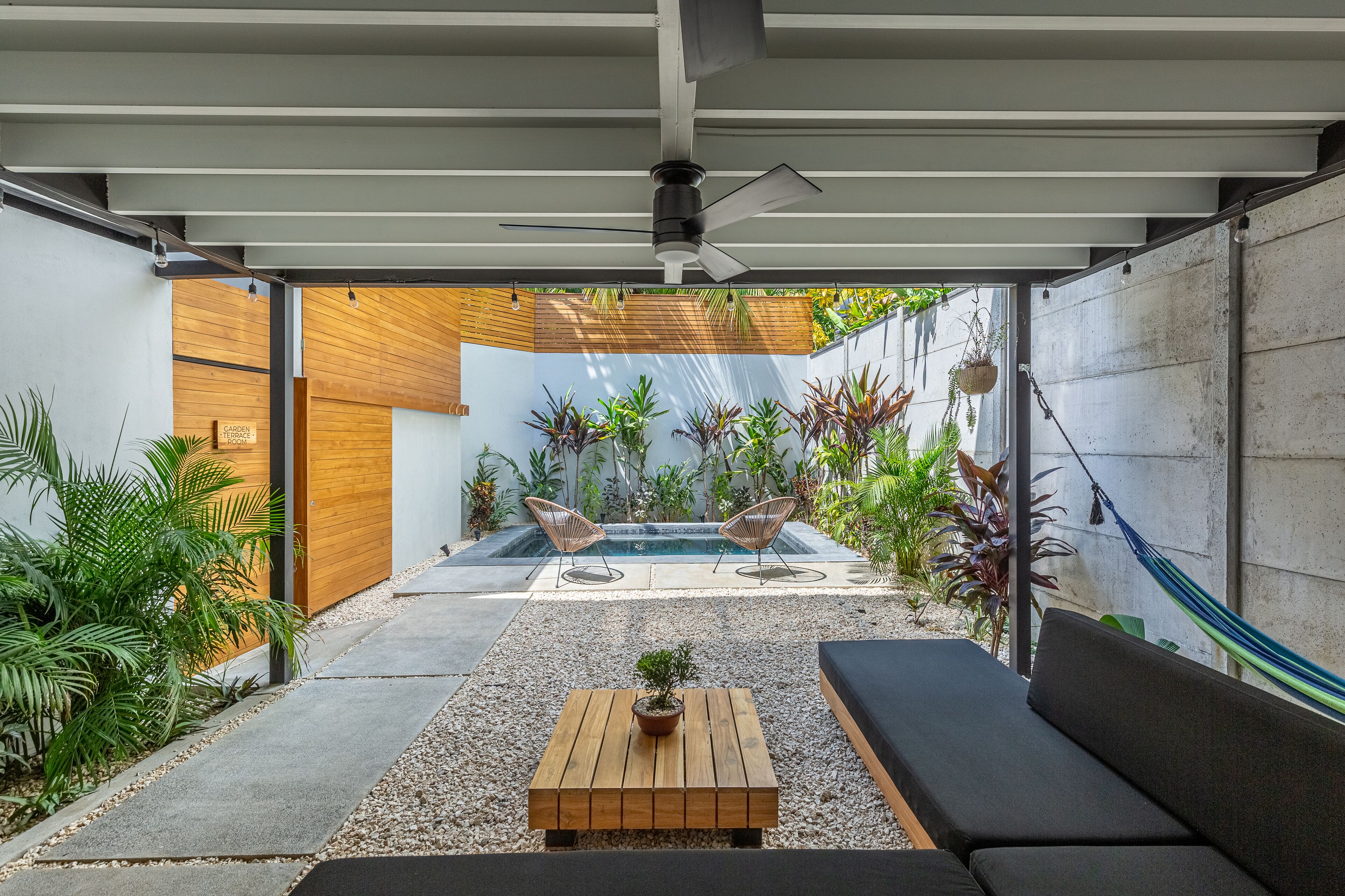 A modern outdoor patio with a pool, seating, and various plants.