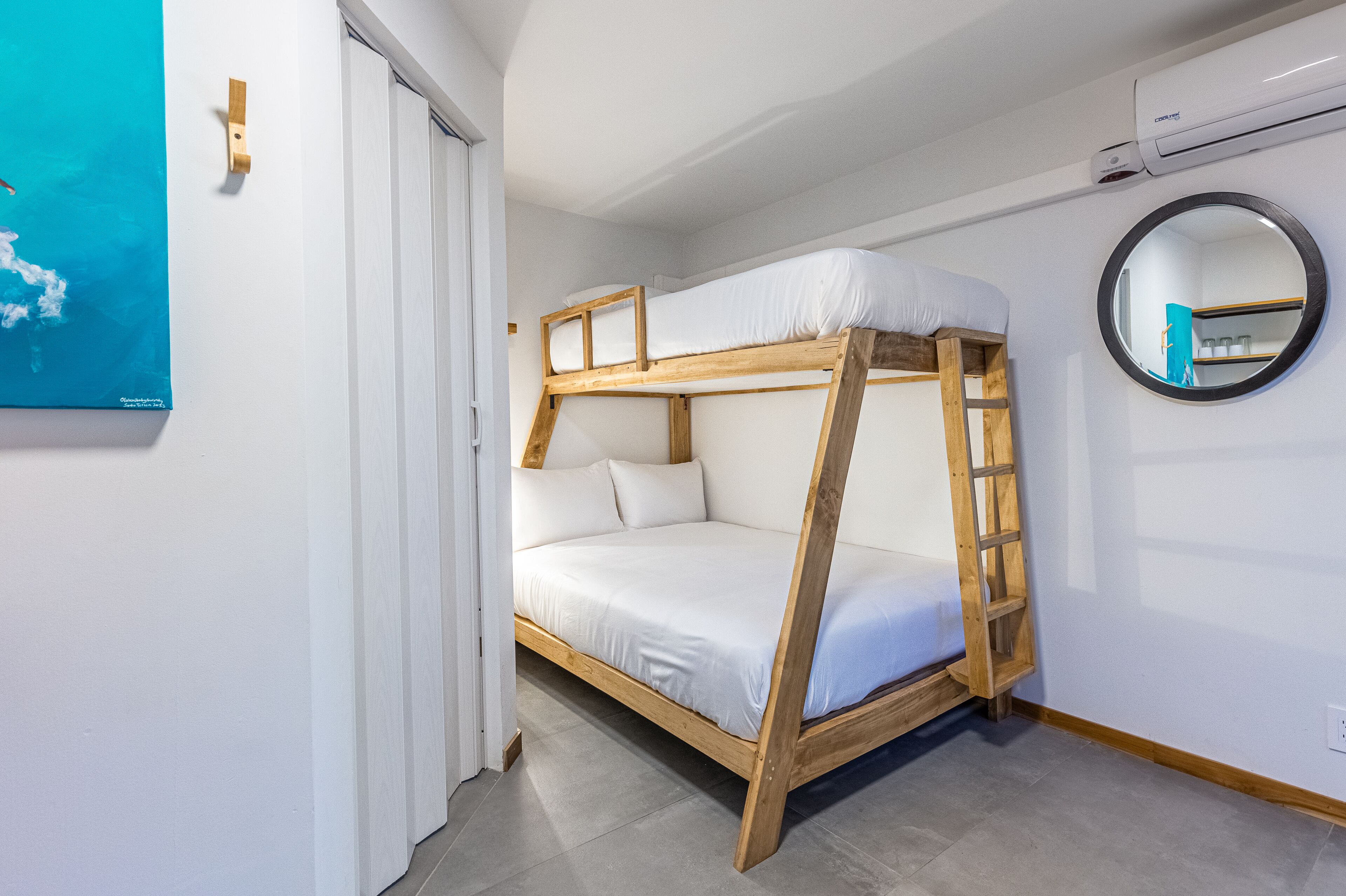 A bunk bed with a wooden frame and white bedding, a round mirror on the wall, and a door with a white frame.