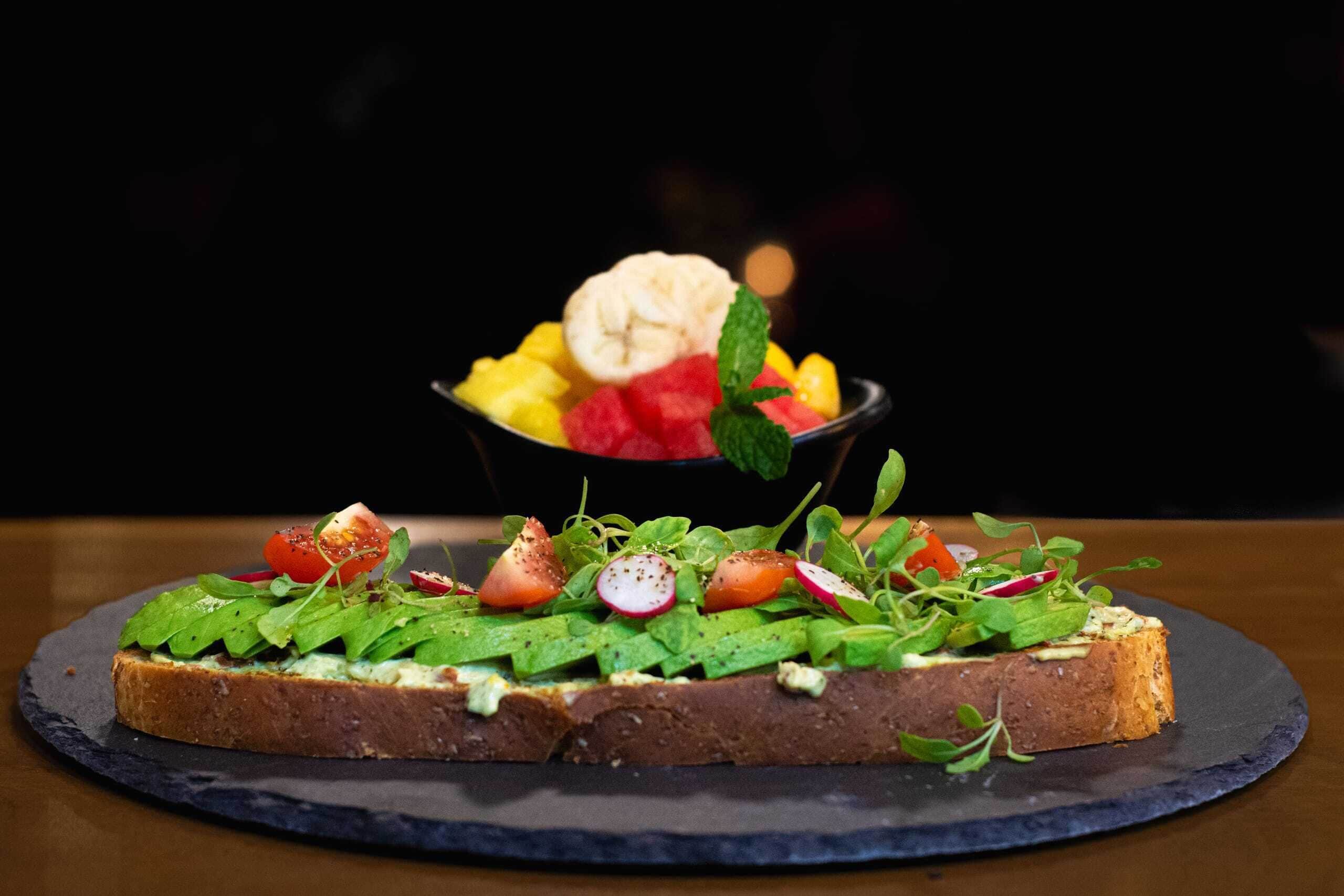 A dessert plate with a slice of bread topped with greens, tomatoes, radishes, and a scoop of ice cream.