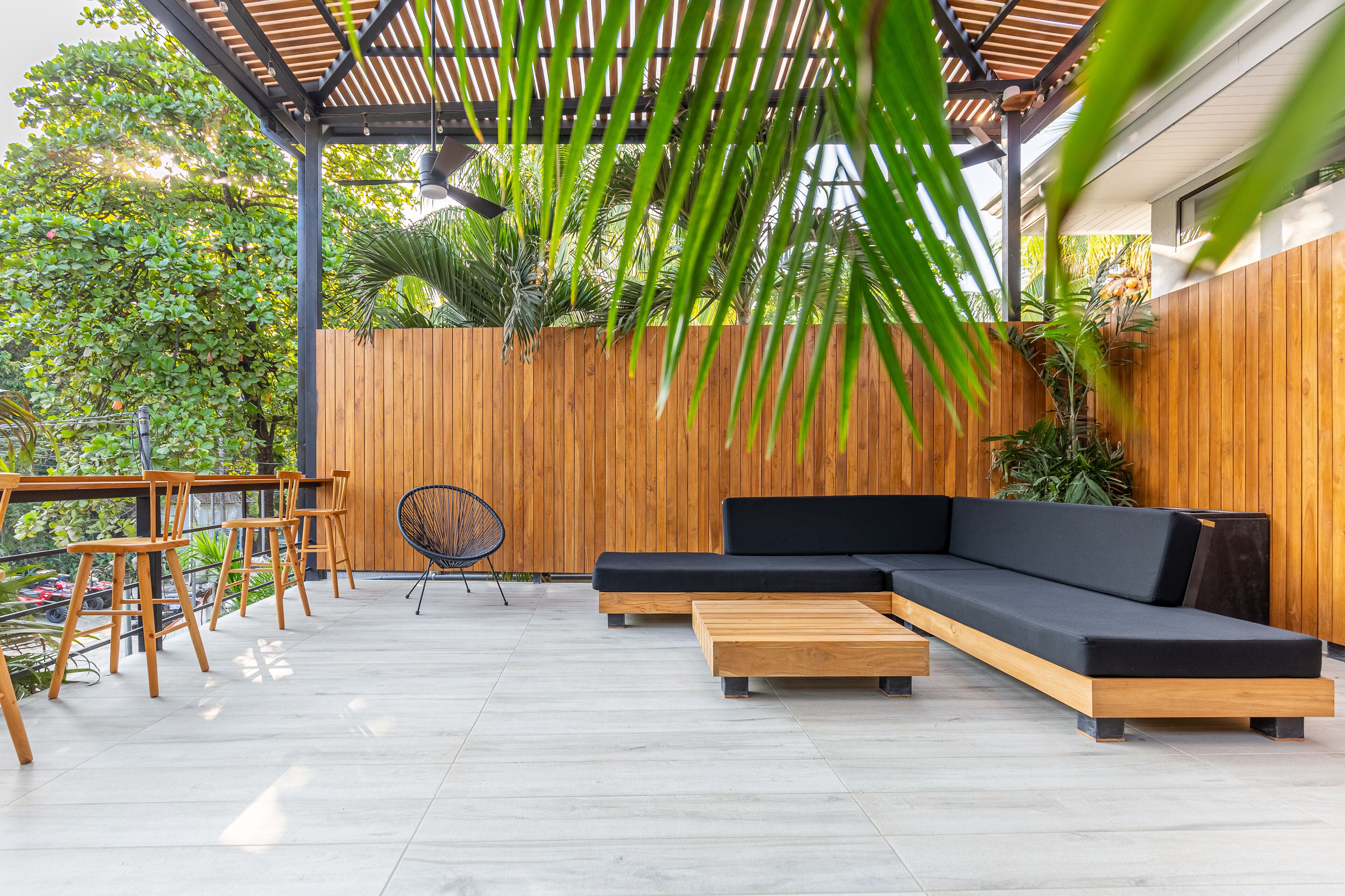 Une terrasse extérieure avec un banc en bois, un canapé noir et une table en bois.