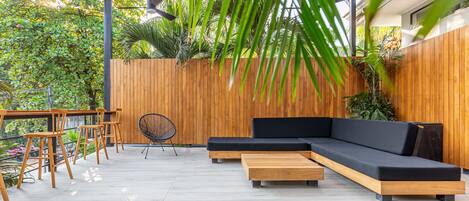 Une terrasse extérieure avec un banc en bois, un canapé noir et une table en bois.
