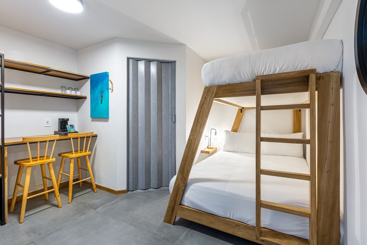 Habitación pequeña con literas, un escritorio y dos sillas de madera, un estante y un armario azul.