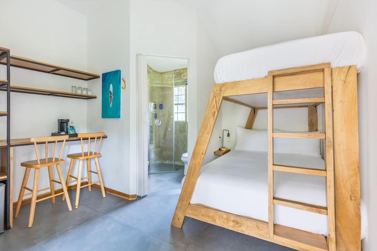 Habitación compacta con literas, un escritorio y dos taburetes, y un rincón de ducha.