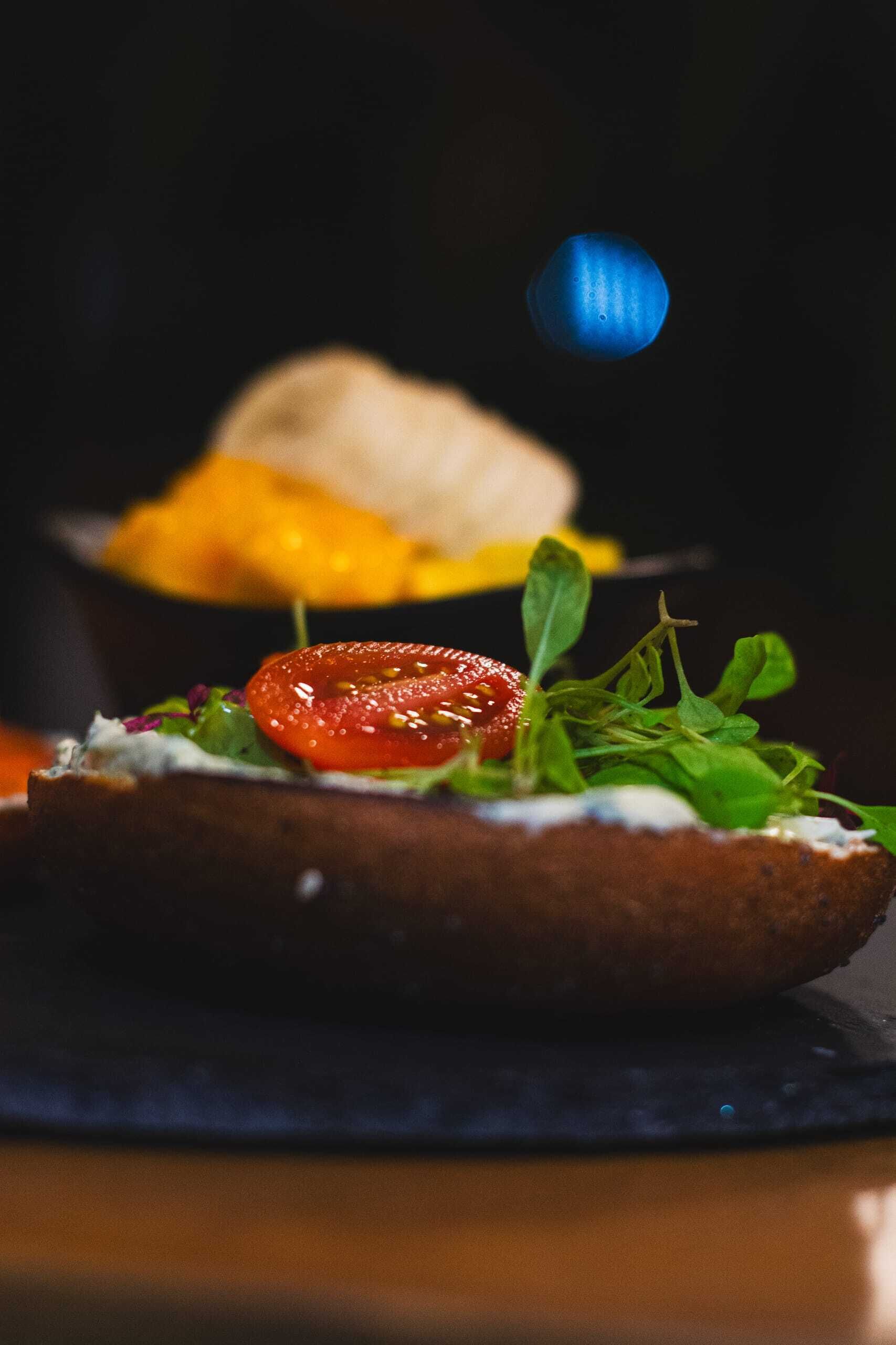 A sandwich with a slice of tomato and greens on a dark plate.