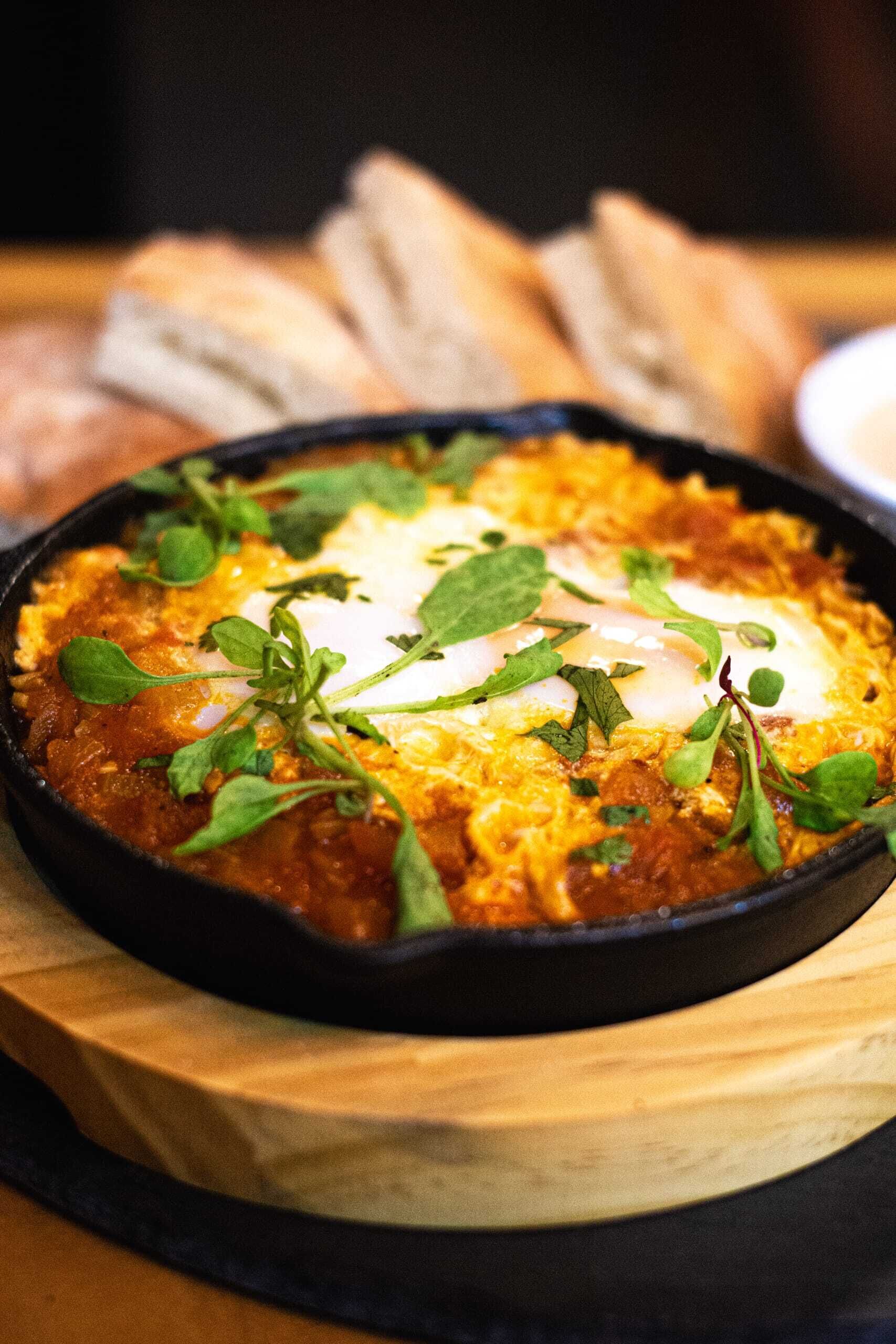 Un plato de sartén con huevos y vegetales sobre una tabla de madera.