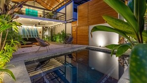 Un espace piscine extérieur moderne doté d’une piscine à fond de verre, d’une terrasse en bois et de chaises longues.