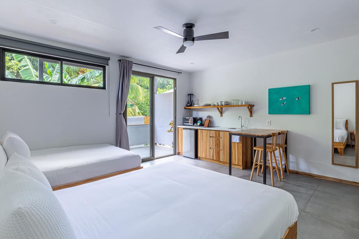 Una habitación de hotel moderna con una cama grande, kitchenette y puerta corrediza al exterior.