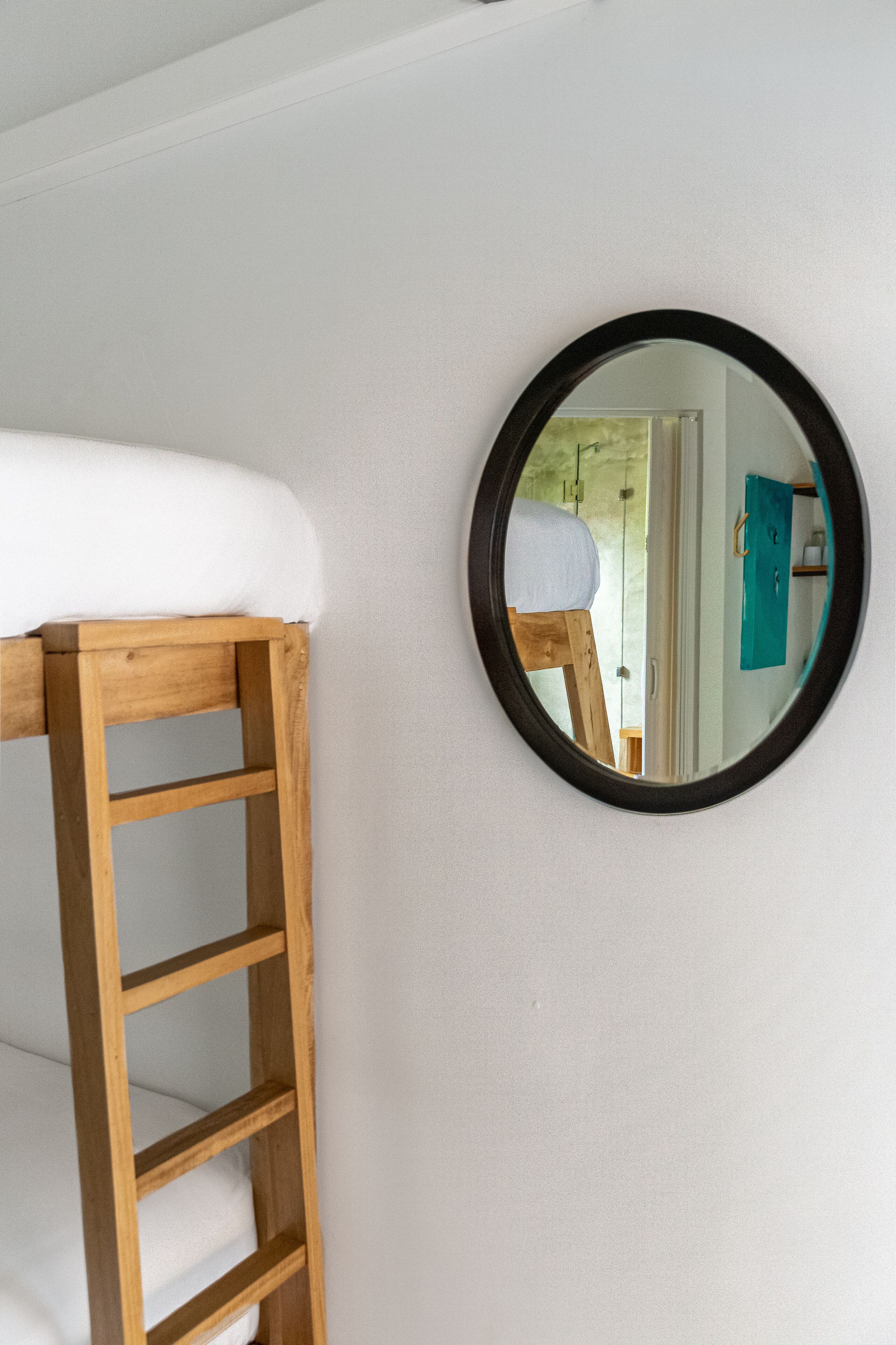 A bunk bed with a wooden ladder and a round mirror on the wall.