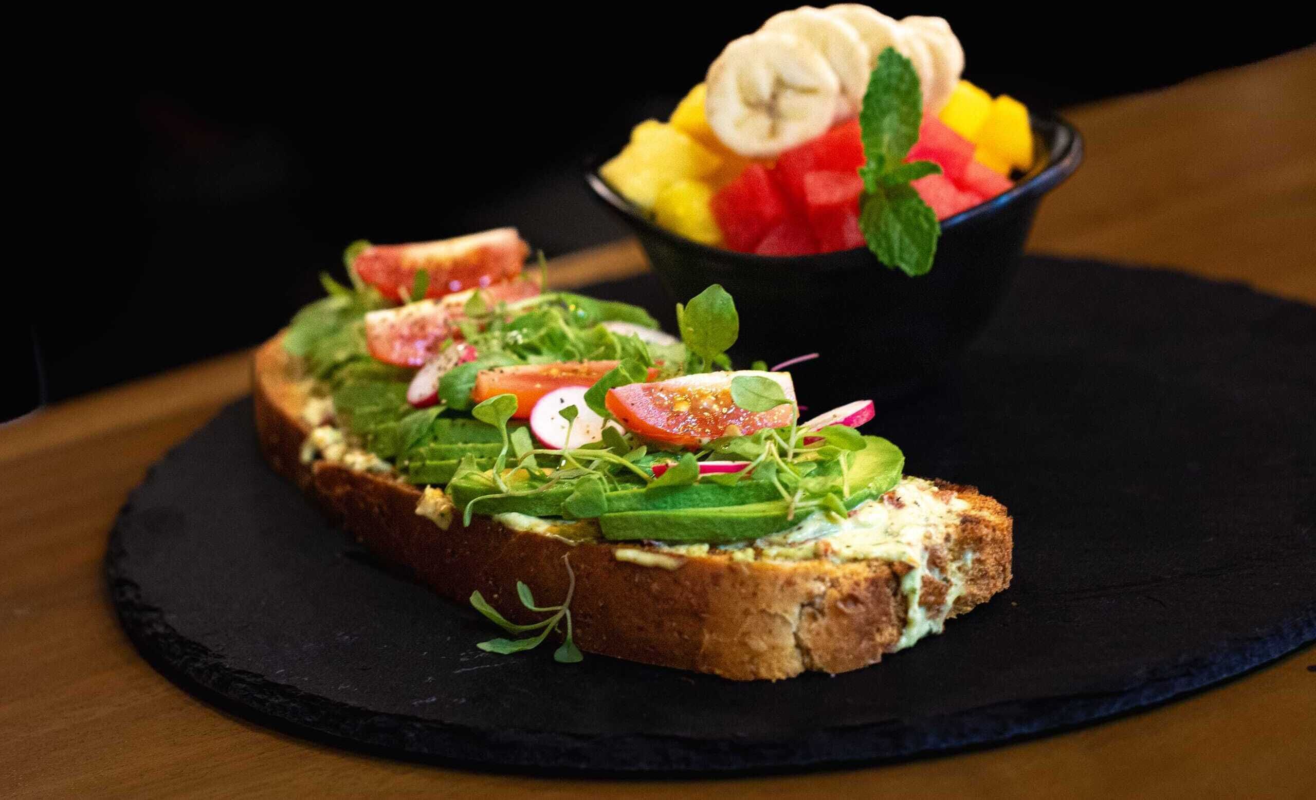 A sandwich with fresh vegetables on a slice of bread, accompanied by a bowl of fruit salad.