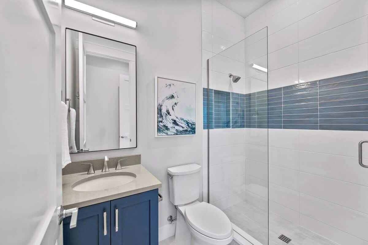 A modern bathroom with a glass-enclosed shower, a white toilet, and a sink with a blue cabinet.