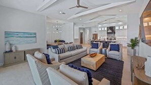 Ein geräumiger Wohnbereich mit einer Couch, Sesseln und einem Couchtisch. Im Hintergrund ist ein Essbereich zu sehen.