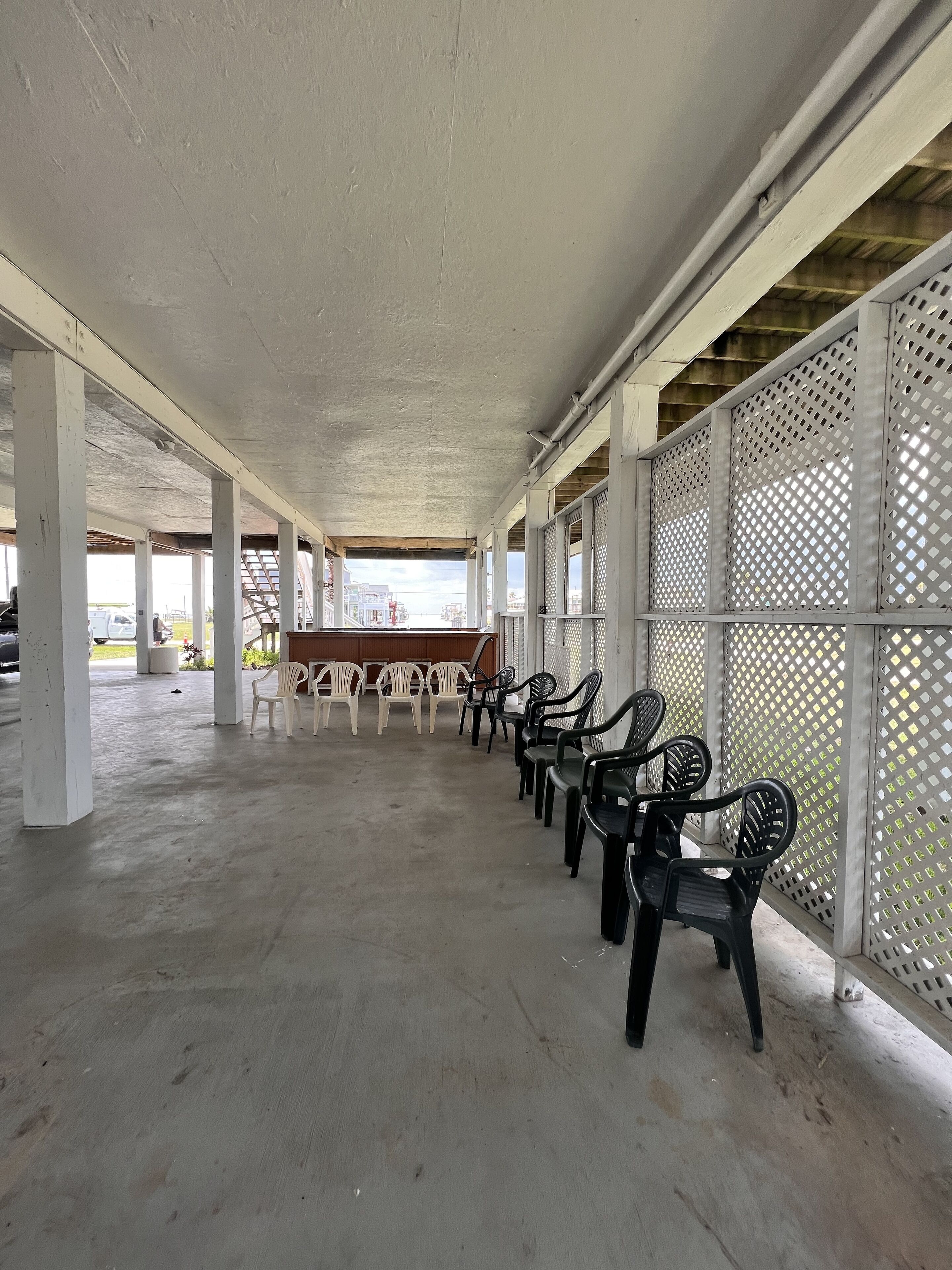 A covered outdoor seating area with rows of plastic chairs and a concrete floor.
