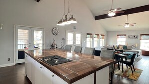 Una cocina amplia con una isla grande, pisos de madera oscura e iluminación colgante.