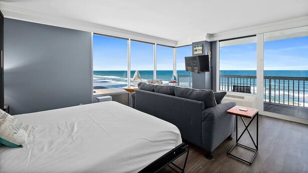 Ett hotellrum med en säng, en soffa, en tv och en balkong med utsikt över havet.