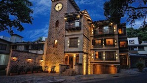 Un edificio de varios pisos con una torre de reloj, balcones e iluminación cálida.