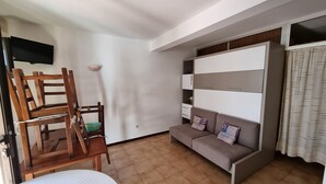 Een woonkamer met een bank, een houten stoel, een tafel en een aan de muur bevestigde televisie.