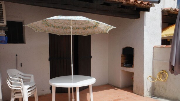 Een terras met een witte tafel en stoelen, een parasol en een betegelde vloer.