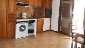 Een compacte keuken met houten kastjes, een ingebouwde oven, een wasmachine en een vaatwasser.