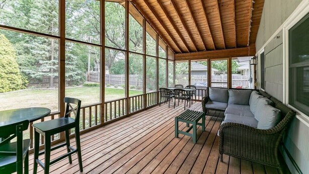Un porche cubierto con piso de madera, una mesa de comedor con sillas, un sofá y un banco.