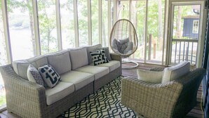 A covered porch with a wicker sofa, a wicker chair, and a patterned rug.