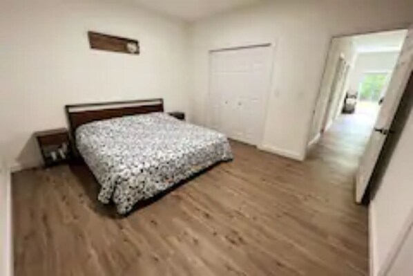 A bedroom with a wooden floor, a bed with a floral bedspread, a nightstand, and a closed door.