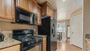 A kitchen with wooden cabinets, a black stove, a refrigerator, and granite countertops. - Townhouse near College of Idaho, workspace (Caldwell)