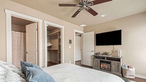 A bedroom with a bed, a ceiling fan, a fireplace, and a TV mounted on the wall. - Townhouse near College of Idaho, workspace (Caldwell)