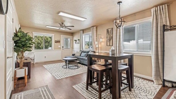 A spacious living room with a dining area, large windows, and a ceiling fan. - Townhouse near College of Idaho, workspace (Caldwell)