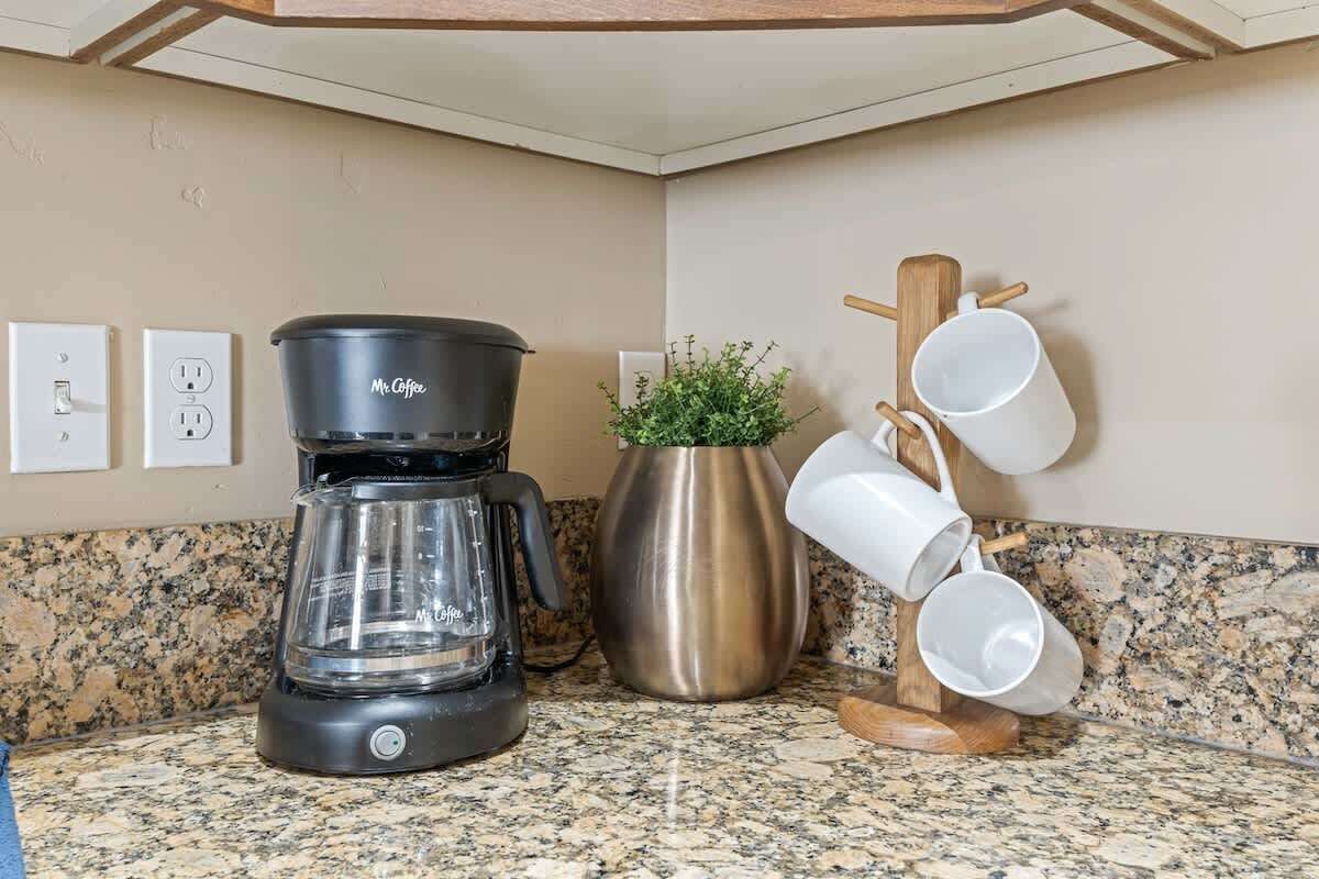 A kitchen with a coffee maker, a potted plant, and a mug rack.