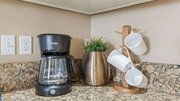A kitchen with a coffee maker, a potted plant, and a mug rack.