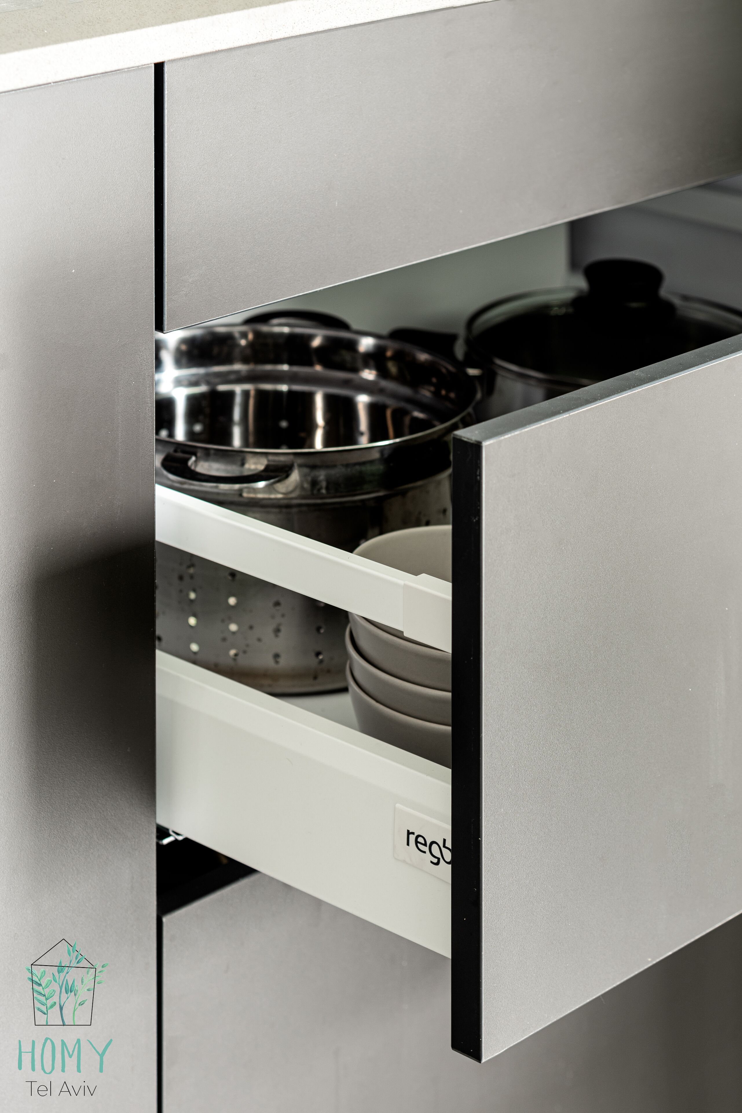 A kitchen drawer with stainless steel appliances, including a colander and pots.