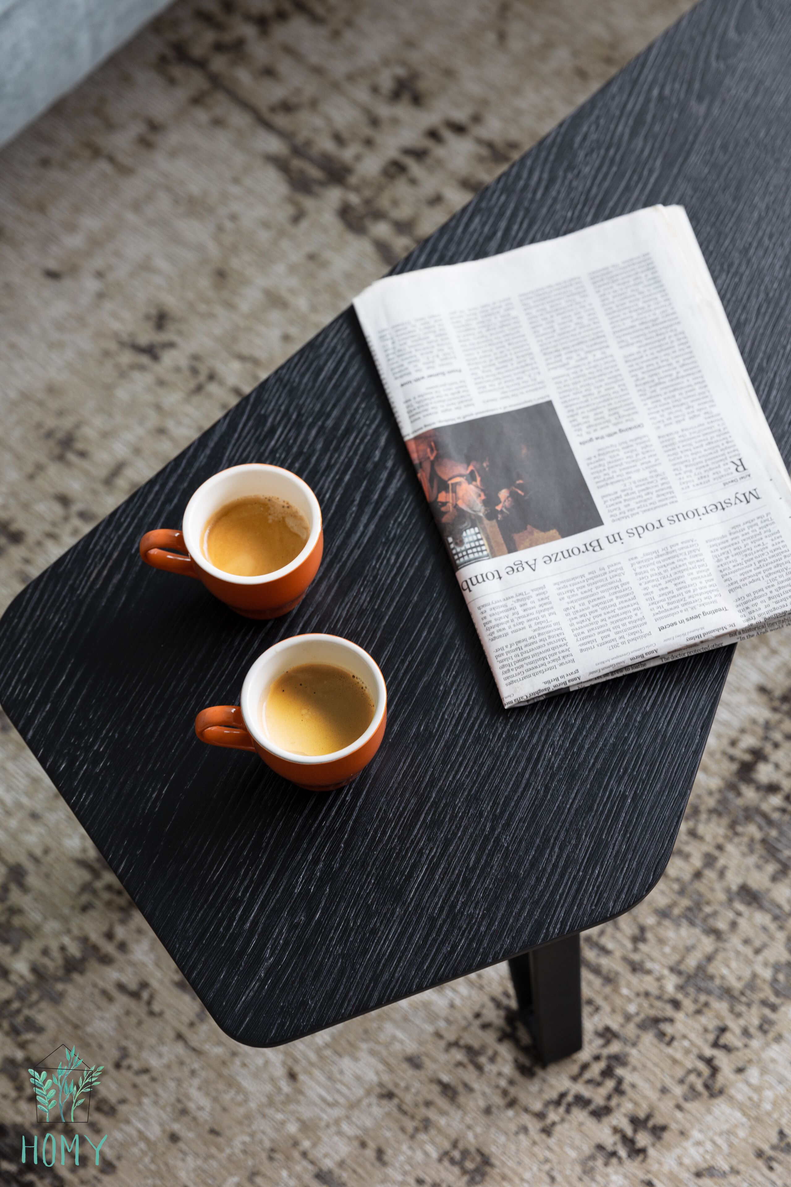 A black table with two coffee cups and a newspaper.