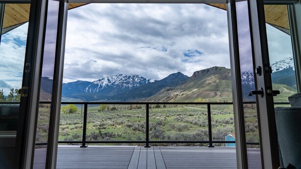 A room with a large window offering a view of a mountainous landscape. - Yellowstone Park Riverfront Chalet (Gardiner)