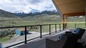 A wooden deck with wicker furniture overlooking a mountainous landscape. - Yellowstone Park Riverfront Chalet (Gardiner)