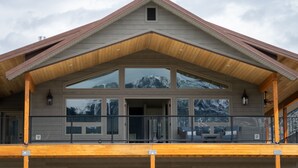 A modern house with a large balcony, a wooden deck, and a mountain view. - Yellowstone Park Riverfront Chalet (Gardiner)