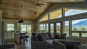 A spacious living area with a large gray sofa and a kitchen with white cabinets. - Yellowstone Park Riverfront Chalet (Gardiner)