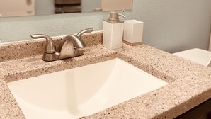 A bathroom with a granite countertop, a sink, a mirror, and a towel rack.