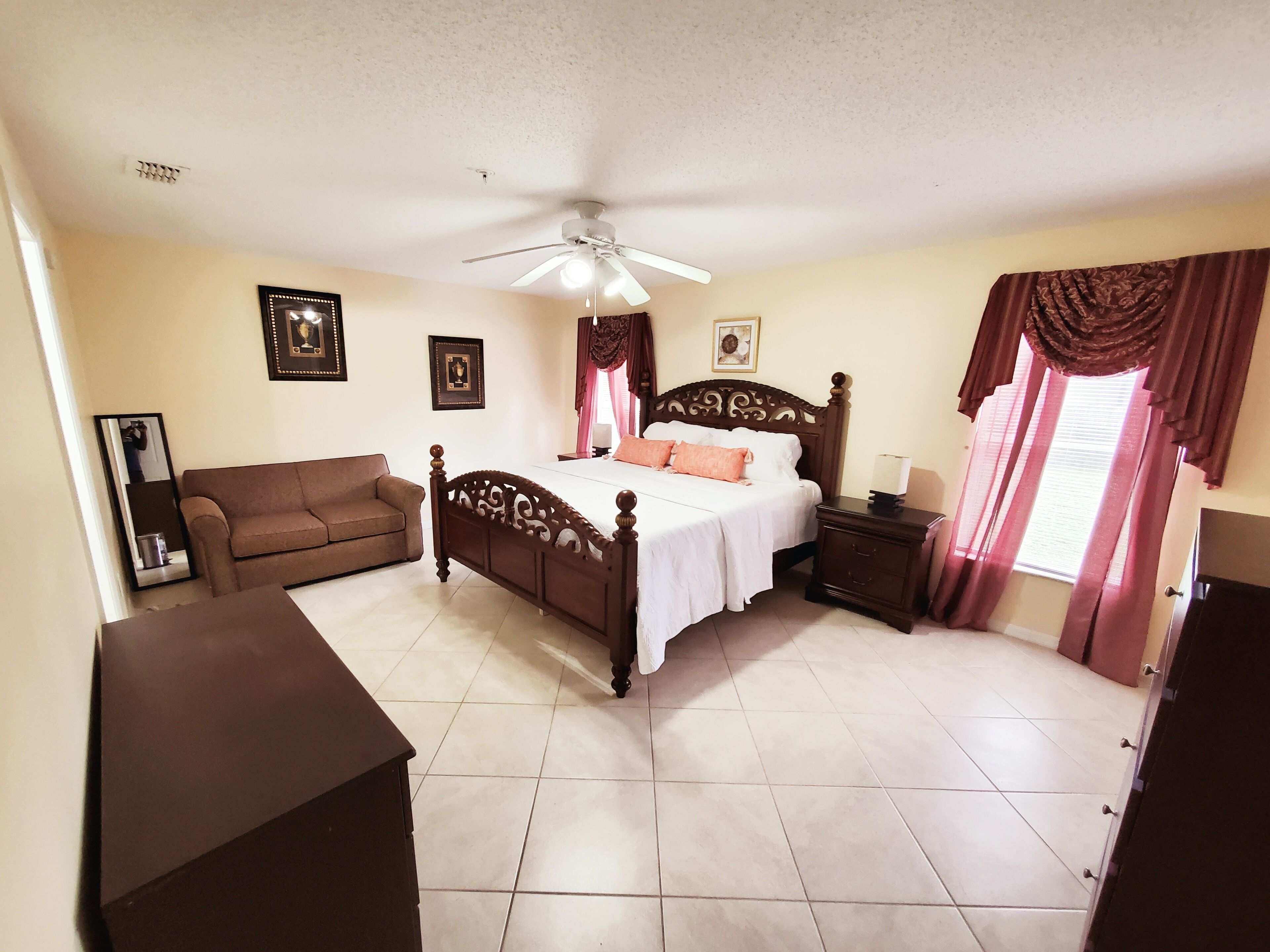 A bedroom with a wooden bed, a brown sofa, a ceiling fan, and a nightstand with a lamp.