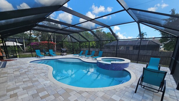 A covered outdoor swimming pool with a hot tub, surrounded by lounge chairs and a patio area. - SERENITY Vacation Home • Heated Pool • Sleeps 12 (Port St. Lucie)