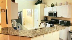 A modern kitchen with granite countertops, white cabinets, a stainless steel range, and a microwave. - SERENITY Vacation Home • Heated Pool • Sleeps 12 (Port St. Lucie)