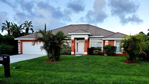 A two-story house with a garage, surrounded by a well-maintained lawn and palm trees. - SERENITY Vacation Home • Heated Pool • Sleeps 12 (Port St. Lucie)
