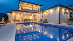 Una casa moderna amb piscina, mobiliari d'exterior i una zona de terrassa ben il·luminada.