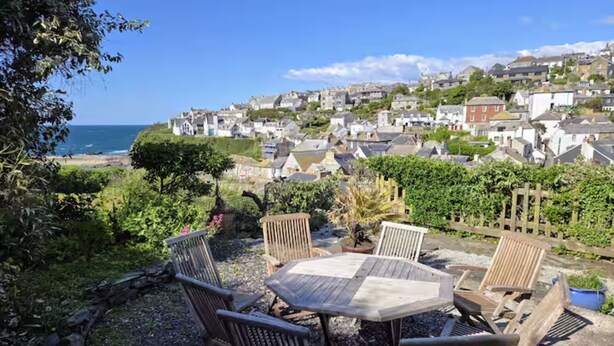 Une terrasse avec une table et des chaises en bois, donnant sur une ville côtière.