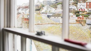 Une vue depuis une fenêtre donnant sur une ville avec des maisons à étages et un paysage vallonné en arrière-plan.