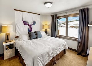 A hotel room with a large bed, two bedside lamps, a window with curtains, and a wall painting of a deer antler.