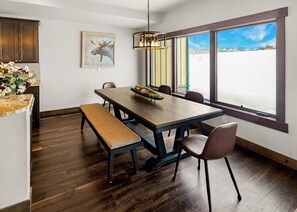 A dining area with a wooden table, benches, and chairs. There is a large window with a view of a snowy landscape.