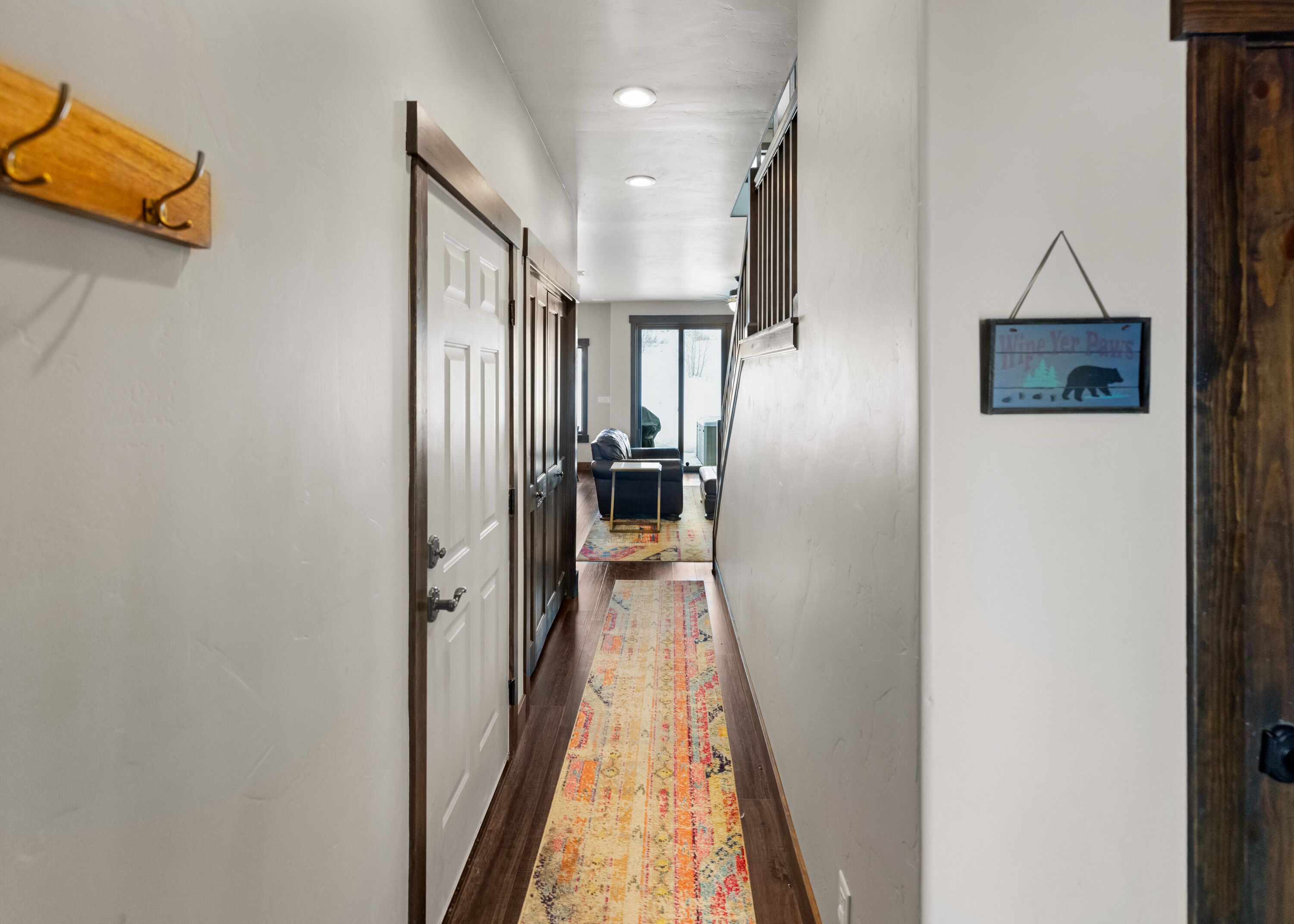A hallway with wooden flooring, white walls, and a door on the left.