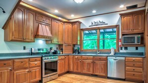 A kitchen with wooden cabinets, stainless steel appliances, and a window with a view of greenery.